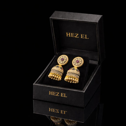 Elegant gold jhumka earrings with ruby detailing by Hezel, showcased in a premium black jewelry box with a luxury finish.