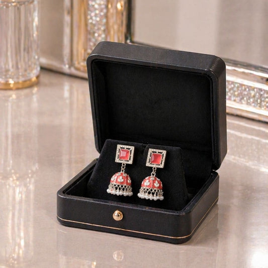 Hezel red jhumka earrings with pearl drops, elegantly presented in a premium black jewelry box on a glossy surface with a luxury background