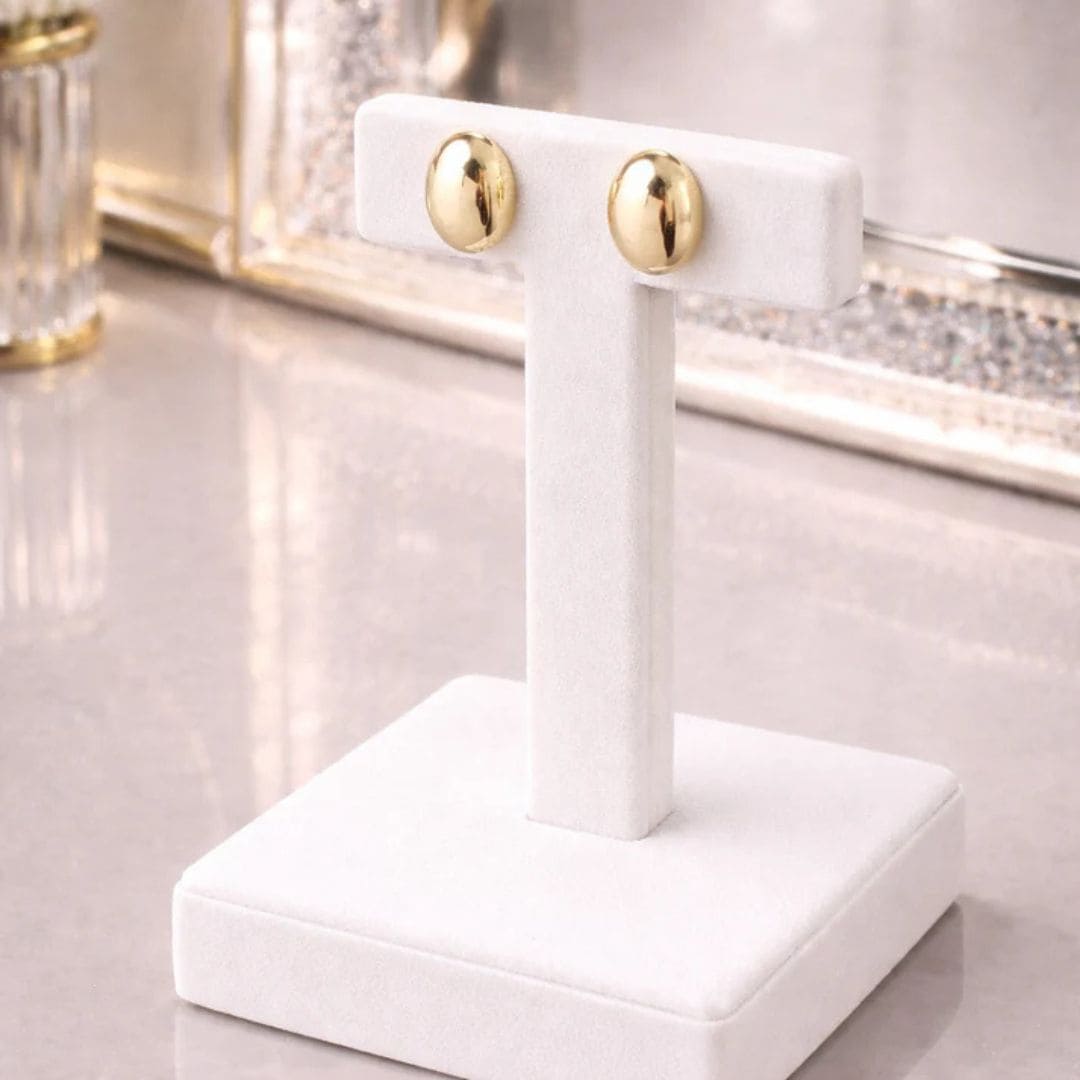 Hezel polished gold stud earrings displayed on a white velvet stand with a luxury background