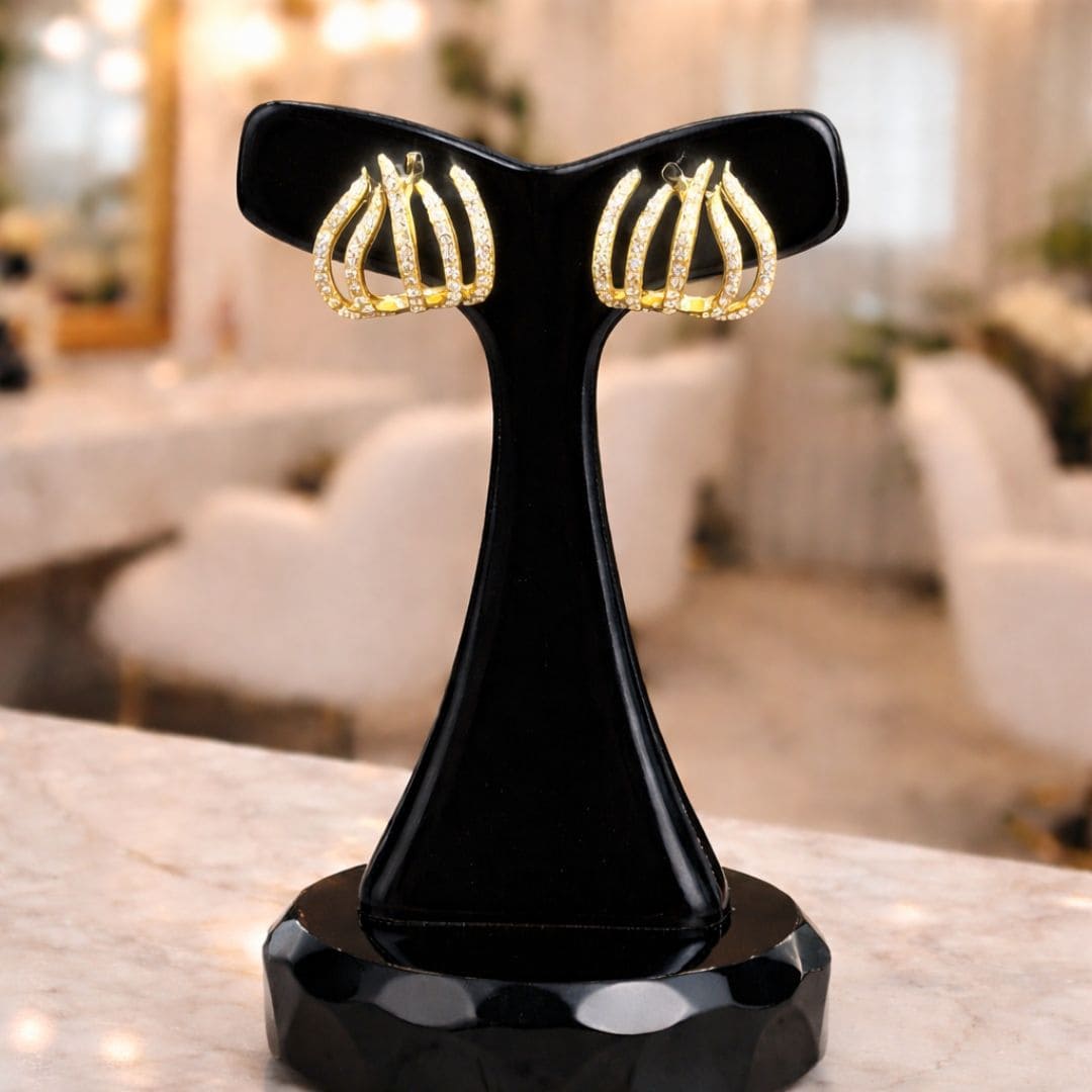 Hezel gold hoop-style earrings with crystal detailing, displayed on a black stand in a soft luxury setting.