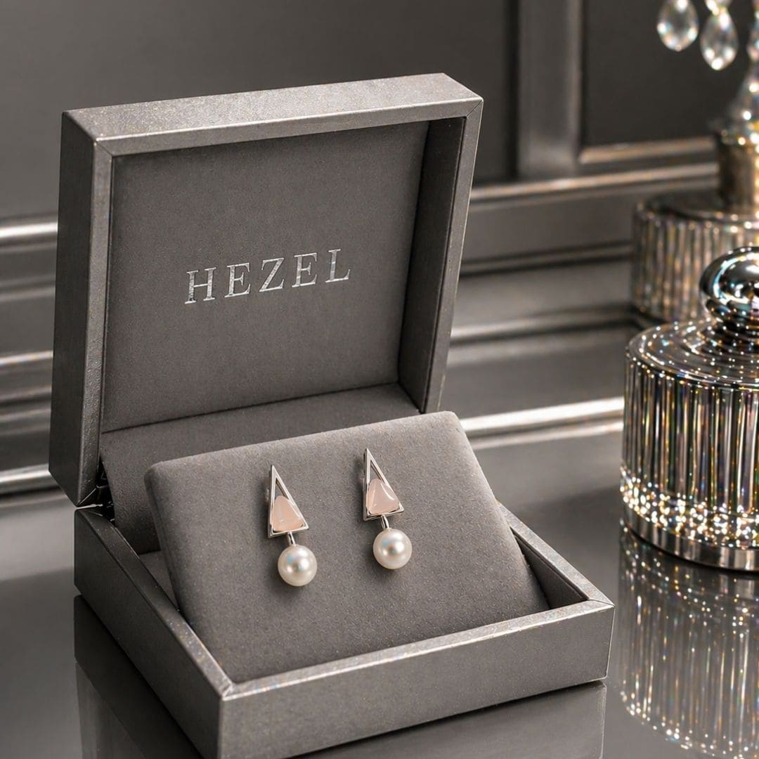 “Hezel triangle stud earrings with pearl drops, elegantly presented in a premium grey jewelry box on a glossy surface.”