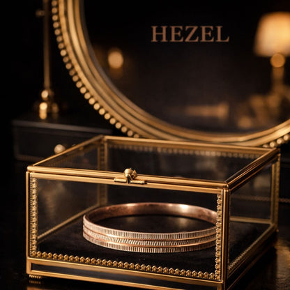 Hezel gold bangle elegantly displayed in a glass jewelry box with a luxurious warm-toned backdrop