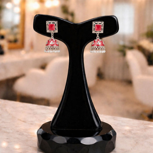 Hezel red jhumka earrings with pearl drops, displayed on a black stand in a soft elegant setting