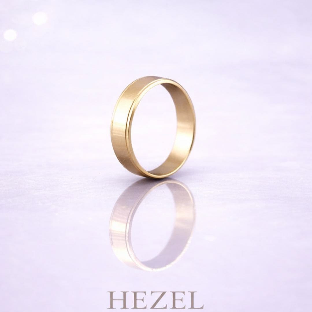 HEZEL minimalist gold band ring displayed on a soft reflective surface with a clean, elegant background, highlighting a timeless and refined desig
