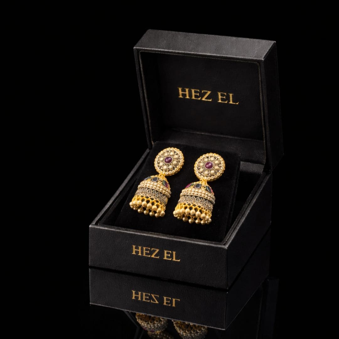 Elegant gold jhumka earrings with ruby detailing by Hezel, showcased in a premium black jewelry box with a luxury finish.