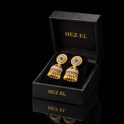 Elegant gold jhumka earrings with ruby detailing by Hezel, showcased in a premium black jewelry box with a luxury finish.