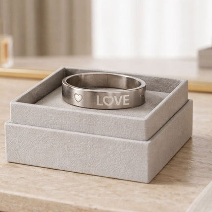 Minimalist silver LOVE engraved ring displayed on a soft-textured luxury jewelry box with a clean, elegant aesthetic