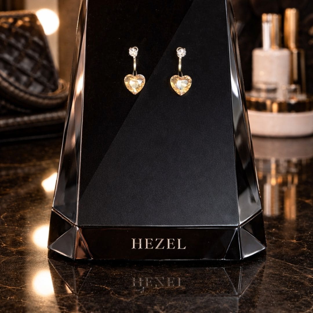 Elegant heart-shaped gold drop earrings by Hezel, displayed on a premium black stand in a luxurious setting.