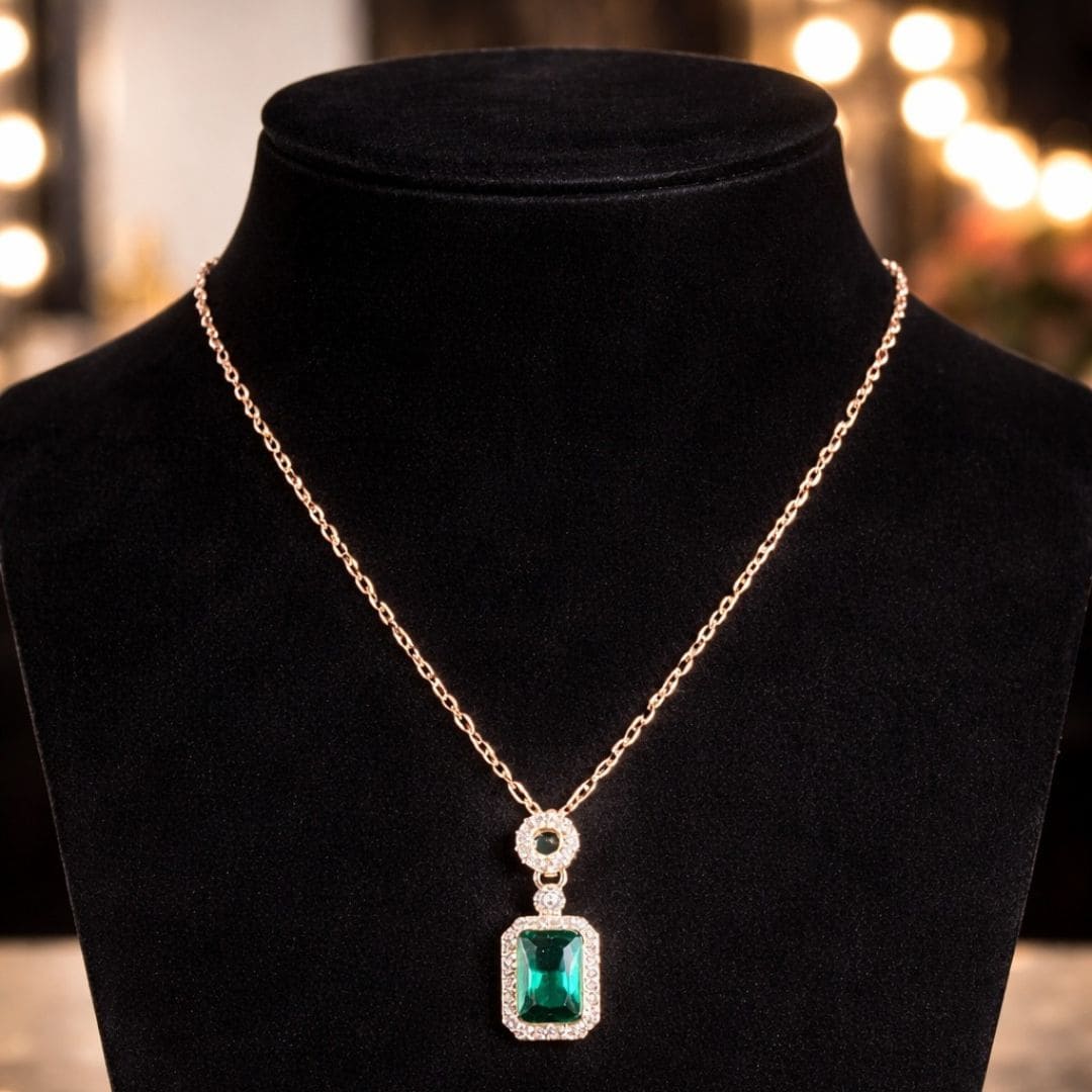Elegant gold necklace with a rectangular emerald-green pendant on a black velvet display, featuring luxury HEZEL branding.