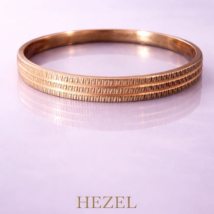 Hezel textured gold bangle showcased on a soft pastel background with a refined minimal aesthetic