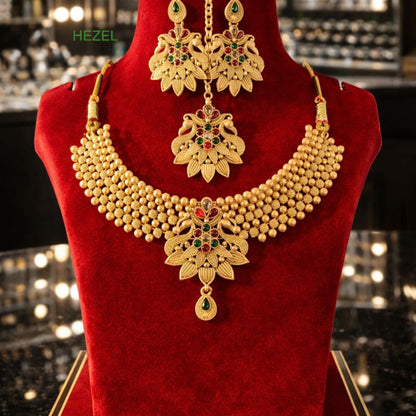 HEZEL gold-tone beaded necklace set with floral motifs, matching earrings, and maang tikka on a premium red display