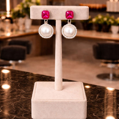 “Red gemstone and pearl drop earrings displayed on elegant beige jewelry stand