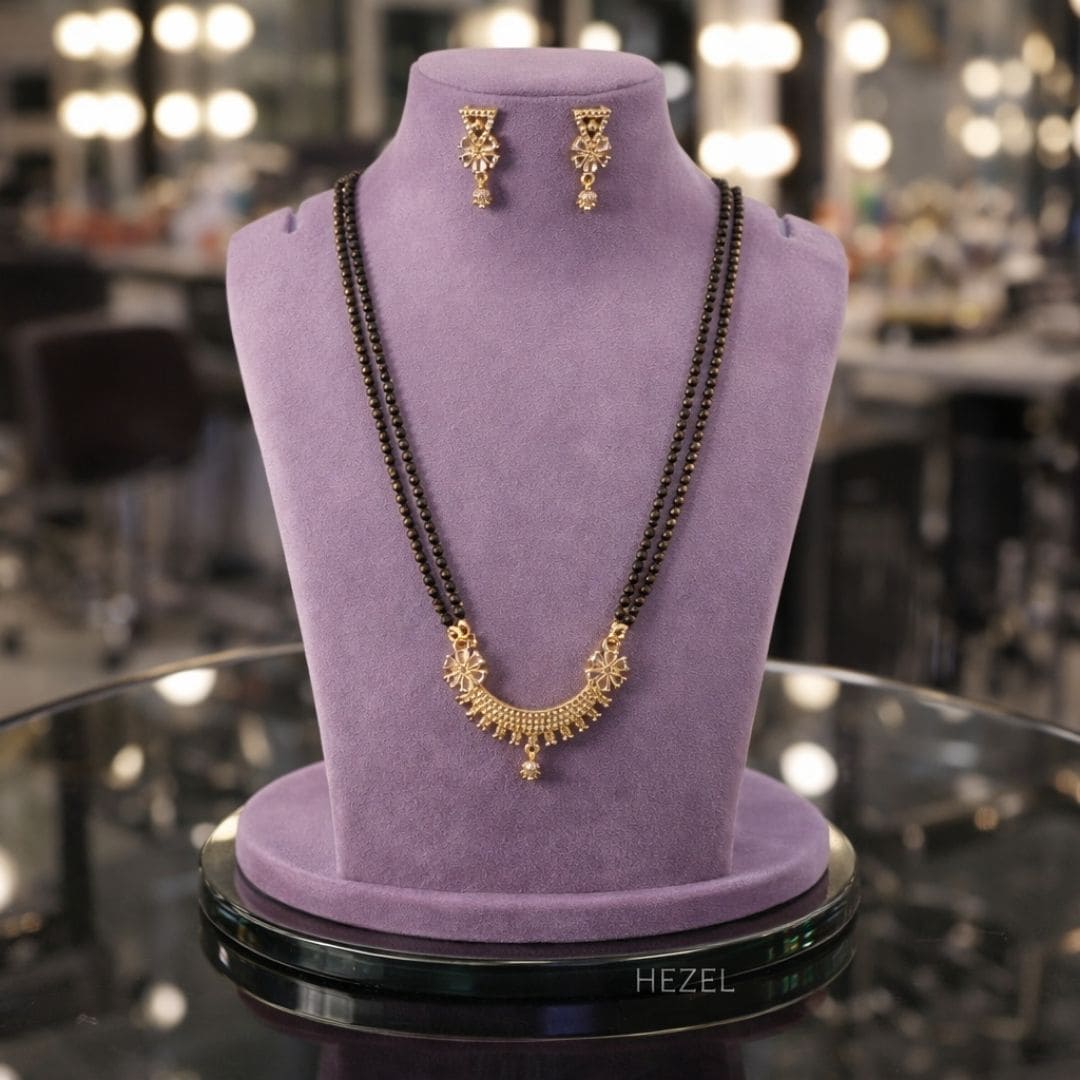HEZEL black bead mangalsutra set with gold pendant and matching earrings, elegantly displayed on a premium lavender jewelry stand